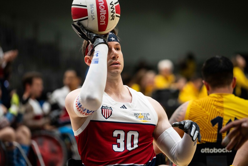 Neczypor, wearing a team uniform, holds up a round ball as players and spectators watch