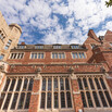 The courtyard-facing red brick facade of Sterling Law Building with the stone tower to the left and evergreen tree to the right and blue cloudy sky above