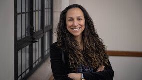 Marisol Orihuela stands next to a window smiling with her arms crossed