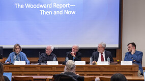 five people seated in front of a screen that says "The Woodward Report — Then and Now"